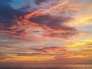 Fiery orange and pink clouds dominate dramatic twilight sky, catching the last light of setting sun above the calm ocean horizon along the picturesque Costa Rican coast, creating a vibrant spectacle