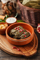 Traditional middle eastern dish dolma. Grape leaves stuffed with rice and meat. Tolma or sarma served in clay bowl with pomegranate seeds and various sauces. Close up view, selective focus