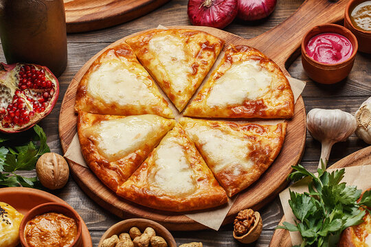 Traditional georgian megrelian khachapuri or megruli on wooden board with sauces, nuts, herbs and vegetables. Close up view