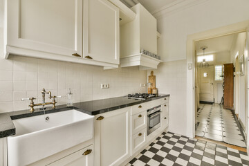 A stylish kitchen showcasing white cabinets, a black countertop, and checkered flooring. Sleek appliances and a light-filled atmosphere create a contemporary feel.