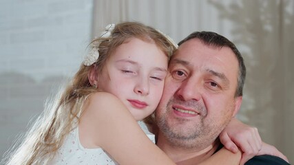 Heartwarming portrait view of young daughter in white gown embracing dad warmly around neck as they smile softly together capturing tender emotional family bond during cozy festive holiday season