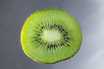 Close-up photo of a fresh kiwi slice on a grey background with backlighting,