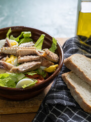 close-up of a mixed salad of lettuce, tomato, egg, and mackerel in a rustic clay bowl with olive oil and natural light