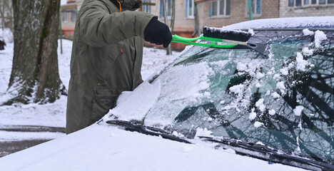a man removes snow from a car. Scraping ice.