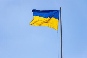Ukrainian Flag Waving Against Clear Blue Sky. Bright blue and yellow Ukrainian national flag fluttering in the wind on a tall flagpole with clear blue sky background.