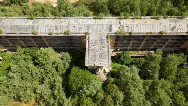Aerial drone footage pulling away from the rooftops of abandoned Prora buildings, revealing their hidden decay amidst forest and sea.
