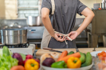 Chef Tying Apron in Professional Kitchen with Fresh Vegetables in Foreground