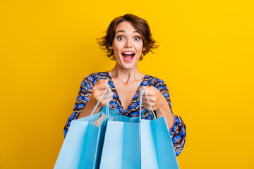 Photo of young overjoyed girl wearing blue blouse open her gifts for birthday with crazy emotions isolated on yellow color background