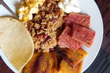 Traditional Costa Rican breakfast, rice and beans, called Gallo Pinto with eggs, tortilla, sausage and plantain.