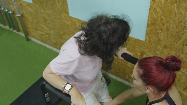 Dedicated woman with cerebral palsy working on strength and mobility, receiving personalized guidance from supportive trainer during adaptive fitness session
