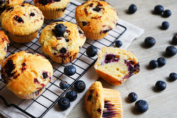 Close-up of vanilla muffins with blueberries on metal mesh tray and cotton towel near blueberries on grey background