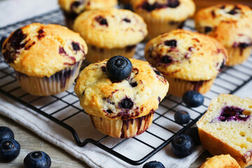 Close-up of vanilla muffins with blueberries on metal mesh tray and cotton towel near blueberries on grey background