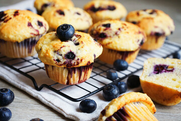 Close-up of vanilla muffins with blueberries on metal mesh tray and cotton towel near blueberries on grey background