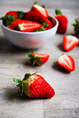 Large ripe strawberries in a white plate next to strawberry berries on a gray wooden table