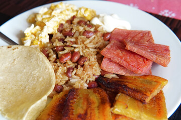 Traditional Costa Rican breakfast, rice and beans, called Gallo Pinto with eggs, tortilla, sausage and plantain.