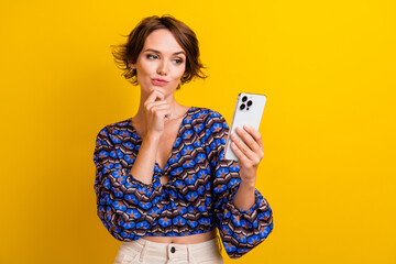 Photo of young thoughtful brown hair lady wearing top using smartphone planning her shopping wish...