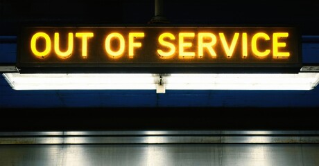 Fototapeta premium Neon out of service sign glowing in dull yellow above subway entrance deep navy and bright silver symbolizing restricted access