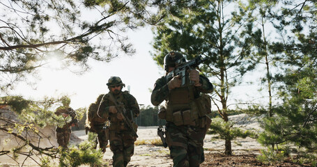 Fototapeta premium Shot from behind bushes, soldiers in camouflage uniforms aim their weapons, patrolling, monitoring the area, securing borders, and training on the firing range in a combat drill.
