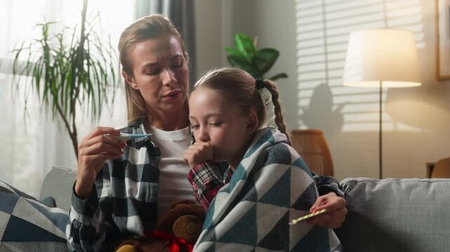Family at home Caucasian mother woman caring hugging ill sick girl child daughter coughing fever mom holding thermometer high temperature check kid drinking remedy medication health problem medicine