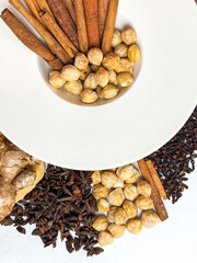 Top view of assorted traditional spices used in Indonesian and Asian cooking,including ginger, turmeric,galangal, cinnamon sticks, cloves, coriander seeds, and candlenuts on white background.