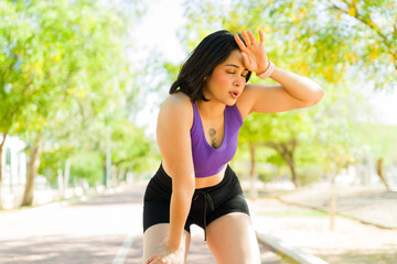Tired runner woman taking break wiping sweat from forehead on running track
