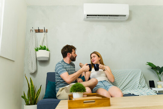 Couple relaxing on sofa under air conditioning, enjoying beverages
