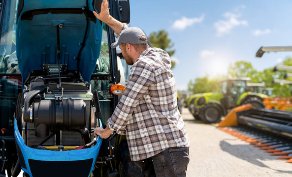 Man inspecting tractor engine with blurred background of agricultural machinery