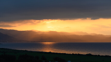 Sunset paints the sky and water with vibrant hues over the mountains and coastline