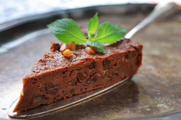 A piece of chocolate cake with nuts on a rustiс plate and decorated with mint. Close up