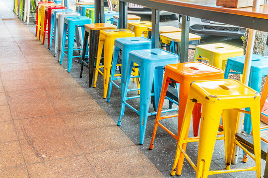 A row of brightly painted metal stools lined up on a footpath