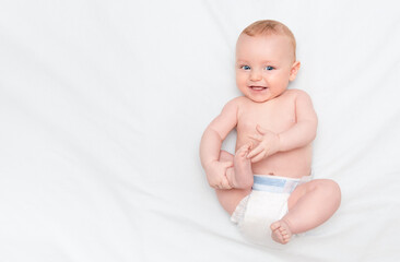 Five month old baby lying on his back, smiling and holding his leg