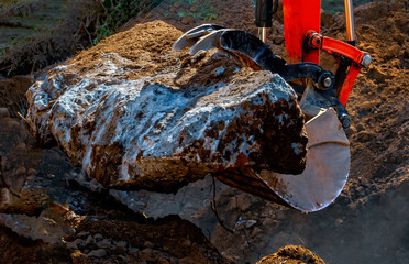 Heavy construction machine, equipped with a claw attachment, lifts a large, irregularly shaped...