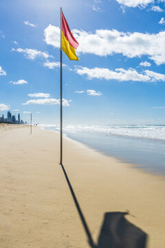 A ground level view along a beach of a lifesaver's flag and its shadow