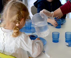 du personnel de cantine sert du pain ou de l'eau à de jeunes écoliers de maternelle ou de primaire