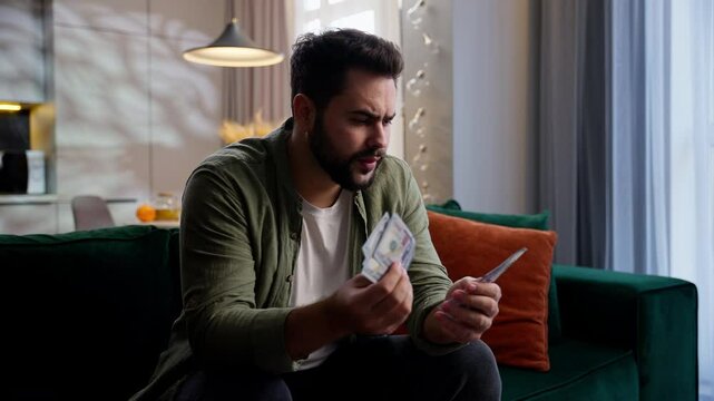 Upset unhappy broke Caucasian business man male guy businessman poor homeowner client sitting sofa counting money lack of cash finance problem savings crisis bankruptcy destitution credit at home room