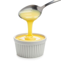 Spoon pouring yellow custard into a white ramekin on a white background in a studio shot