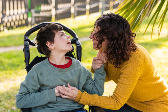 Mother holding hands with son with disability in wheelchair in park