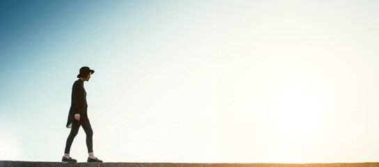 young girl in black clothes and a hat stands against the blue sky. philosophical symbolic path to future. Long horizontal banner template empty copy space. Free spirit concept. sad thoughtful emotions