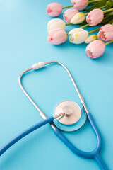 Chestpiece of medical stethoscope and bouquet of tulips on blue background. Vertical greeting card for Doctors or Nurses Day. Selective soft focus and copy space