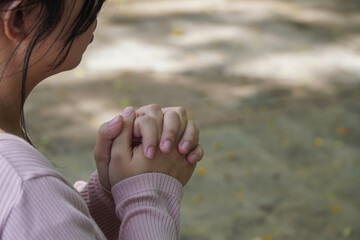 Close up of Woman's Hands Folded in Prayer with Soft Natural Light in a Peaceful Outdoor Setting with Bokeh