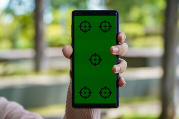 Hand Holding Green Screen Mobile Phone With Target Reticle Mockup on Blurry Green Background During Daylight