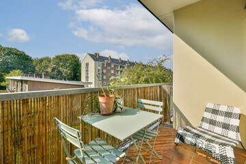 A bright and inviting balcony featuring a green table and chairs, adorned with plants, overlooking a scenic city landscape and blue sky.