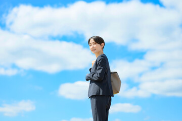 青空バックに立つスーツを着た女性