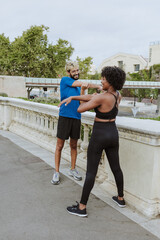 multiethnic couple of friends stretching before running training wearing athletic clothing in a City Park in Spain Europe. Hispanic man and afro hair woman exercising together