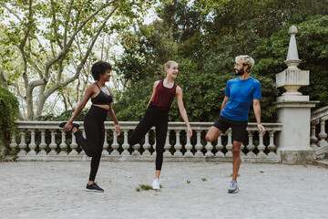 multiethnic friends in their 30s, including men and women wearing athletic clothing doing dynamic stretches together in a City Park in Spain Europe. Hispanic people and afro hair woman