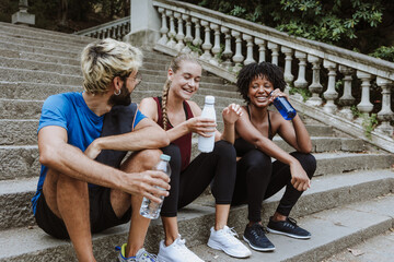 group of multiethnic friends drinking water or coffee and resting after doing exercise together in a City Park in Spain Europe. Hispanic man and afro hair woman wearing athletic clothing
