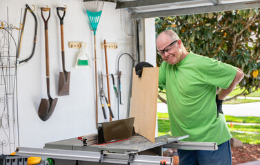 Senior man experiences backache while woodworking in a garage during hobby time. - series