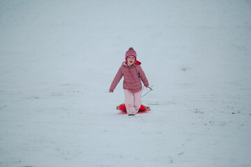 girl in a pink snowsuit running with the sled on a snowy hill