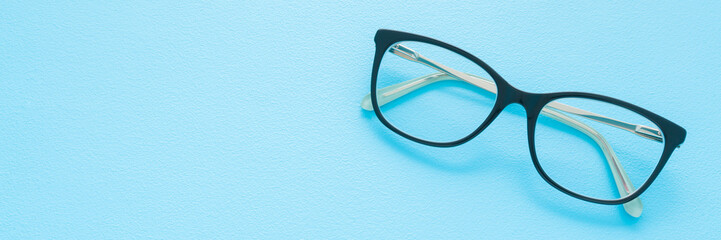 Eyeglasses with dark black plastic frame on light blue table background. Pastel color. Wide banner. Closeup. Empty place for text. Top down view. © fotoduets
