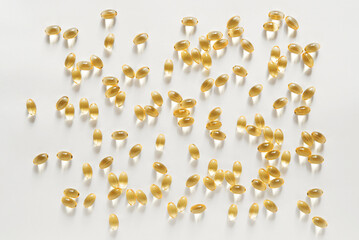Many transparent orange colored oval shaped capsules scattered on a white background, omega 3 fish oil, lecithin, vitamin D	